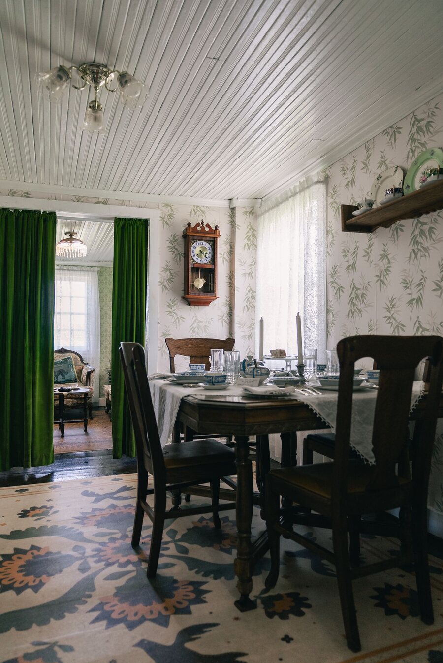 Traditional dining room with subtle floral wallpaper, green drapes and warm light