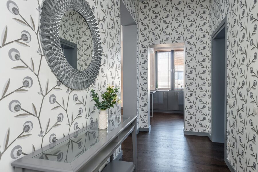 Hallway lined with delicate peacock-feather wallpaper, a round mirror and console table