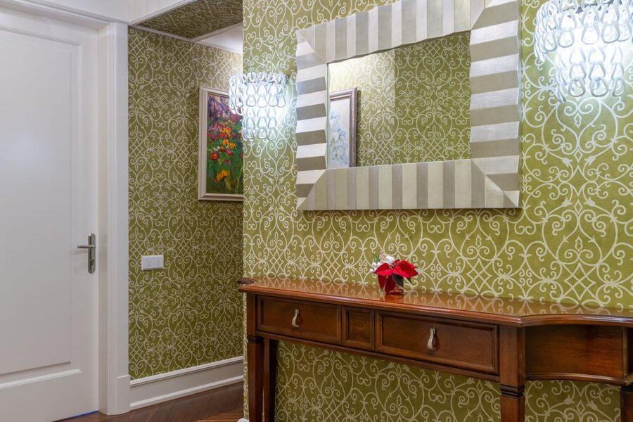 Entry vignette in a green damask wallpaper with a wooden console and mirror