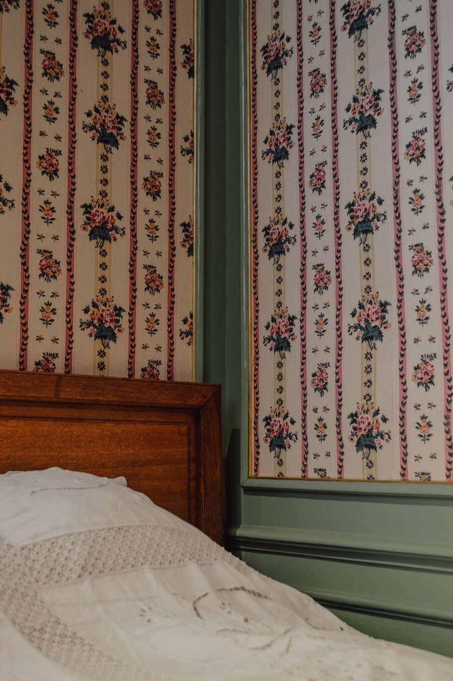 Cozy bedroom corner with a vintage striped floral wallpaper and wooden bed frame