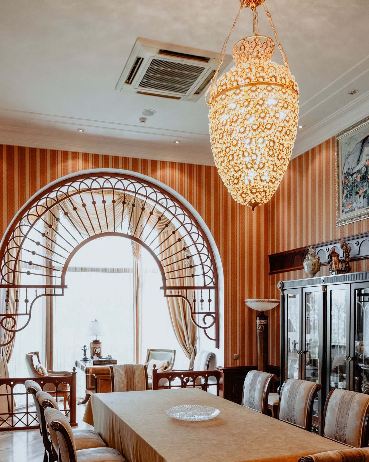 Elegant Chillicothe dining room with terracotta striped wallpaper, an arched window and a crystal chandelier