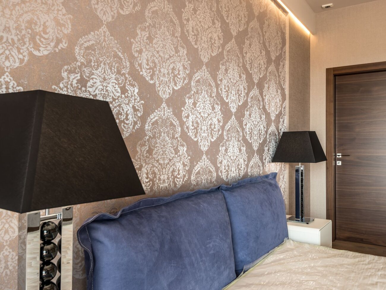 Warm champagne damask wallpaper on a feature wall behind a blue velvet sofa